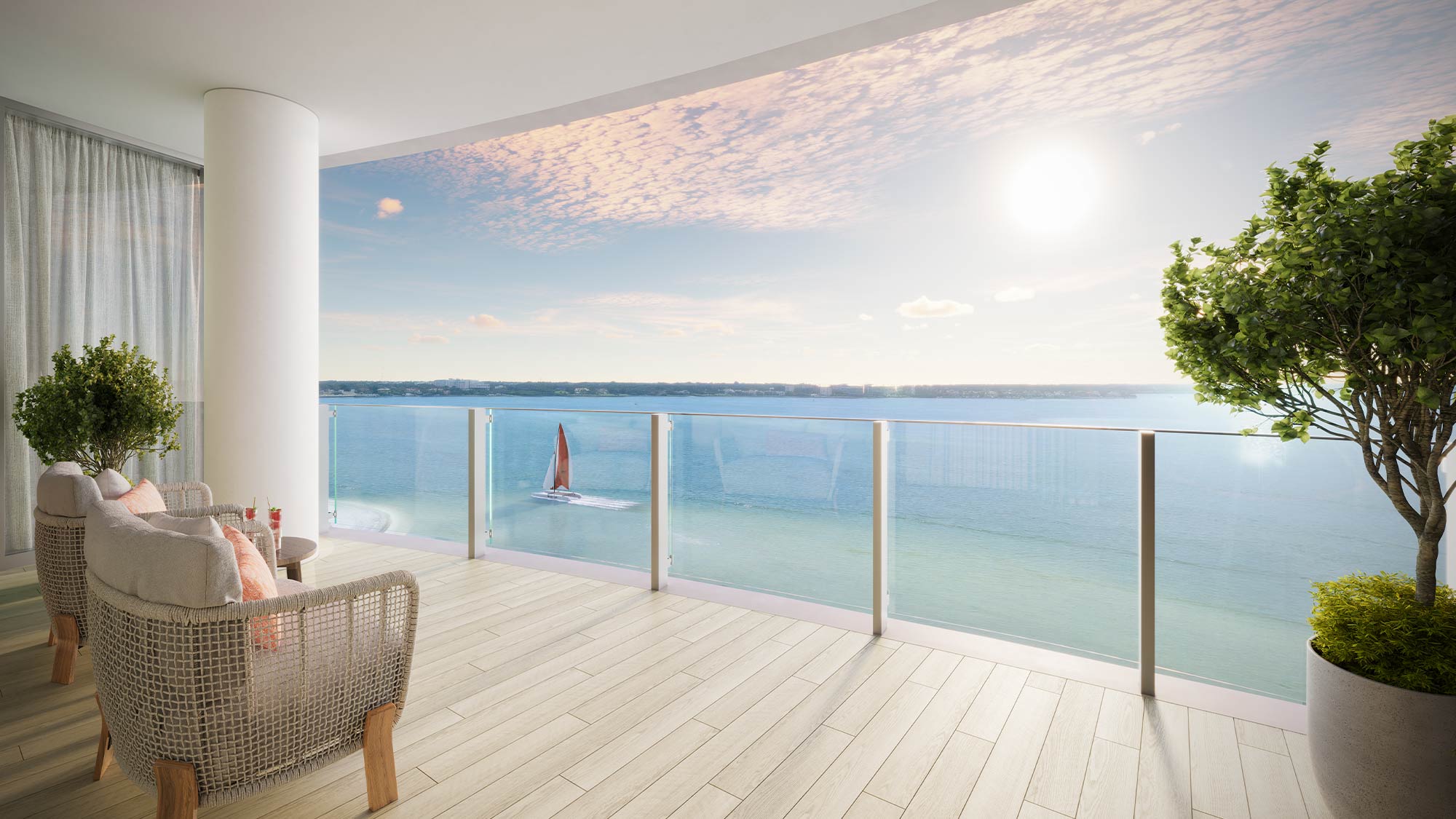 Balcony with glass railing overlooking a calm bay with a sailboat under a bright sky, potted plants and chairs.