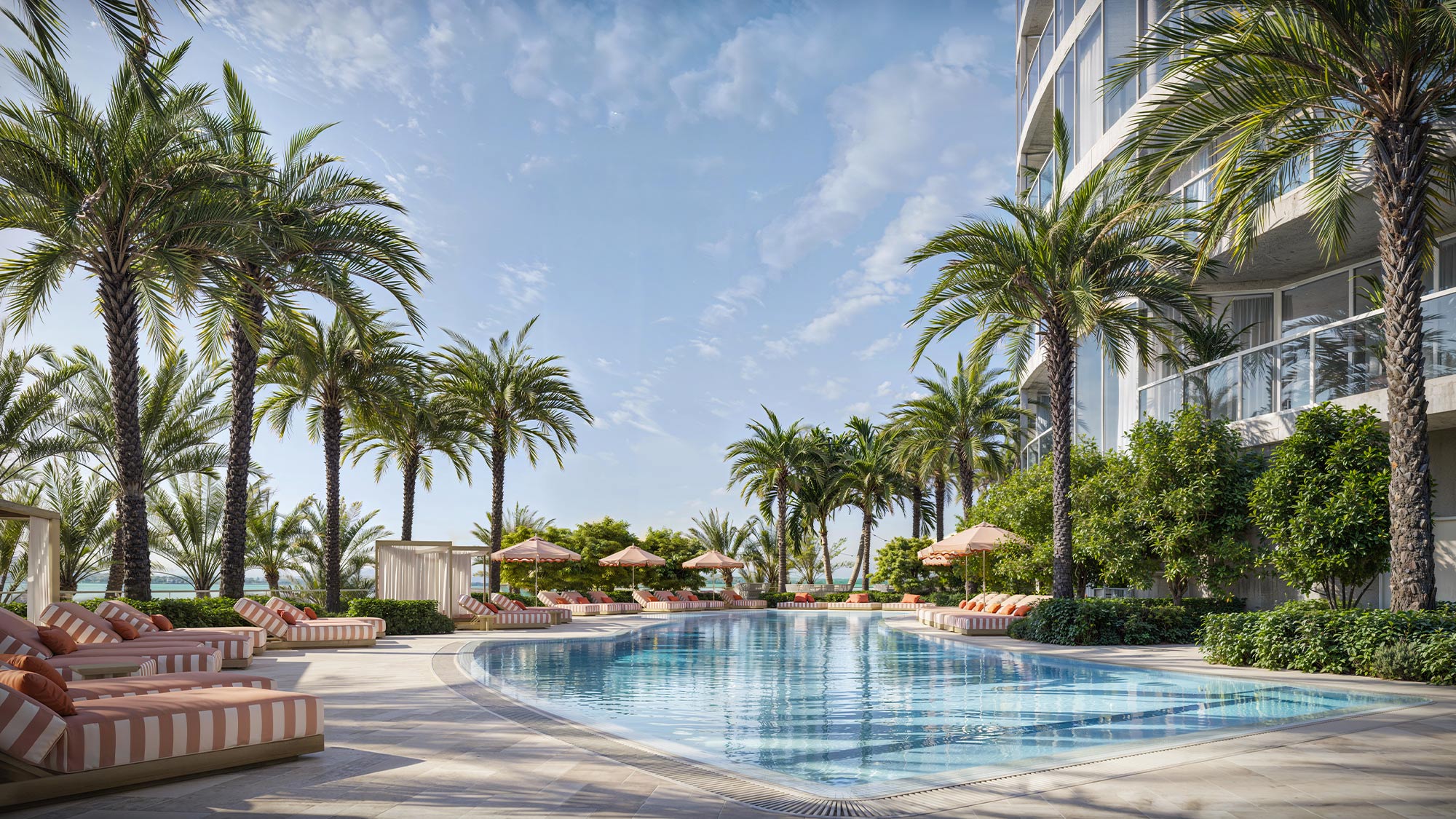 Resort-pool-with-lounge-chairs,-striped-cushions,-tall-palms-surrounding-water,-residential-building-visible,-bright-sky-above