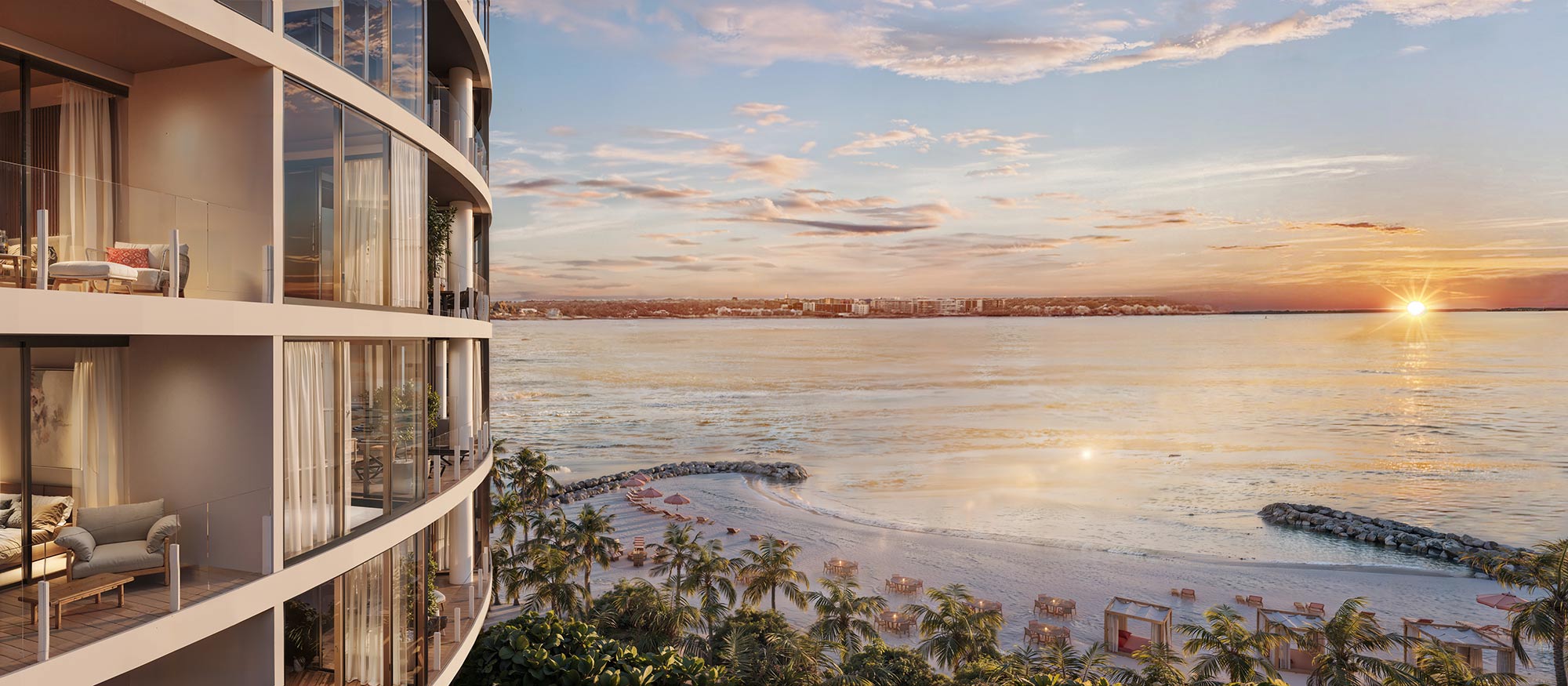 Sunset oceanfront view from high-rise balconies, golden glow over calm water, sandy beach with palms, loungers, rock jetties below